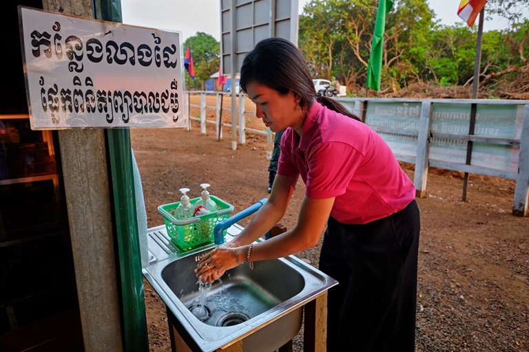Water A woman bends over an outdoor sink to wash her hands.